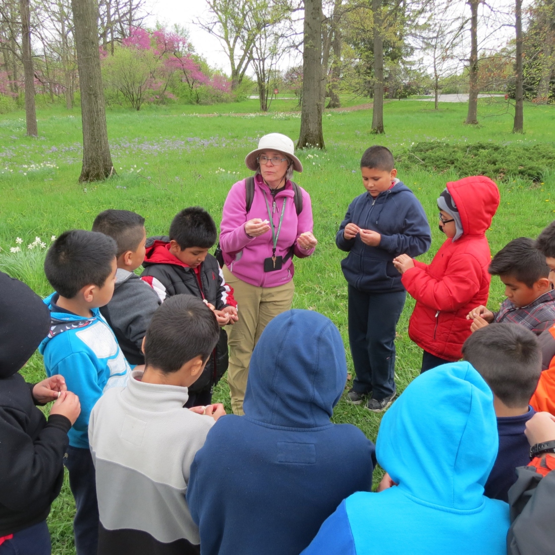 Group of young students surrounding a teacher outside in spring