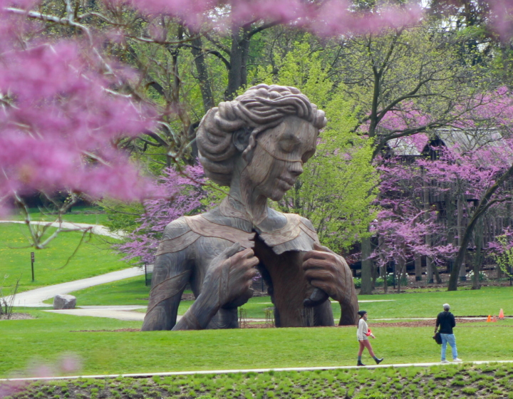 A large sculpture of a woman towers over people walking on a path.