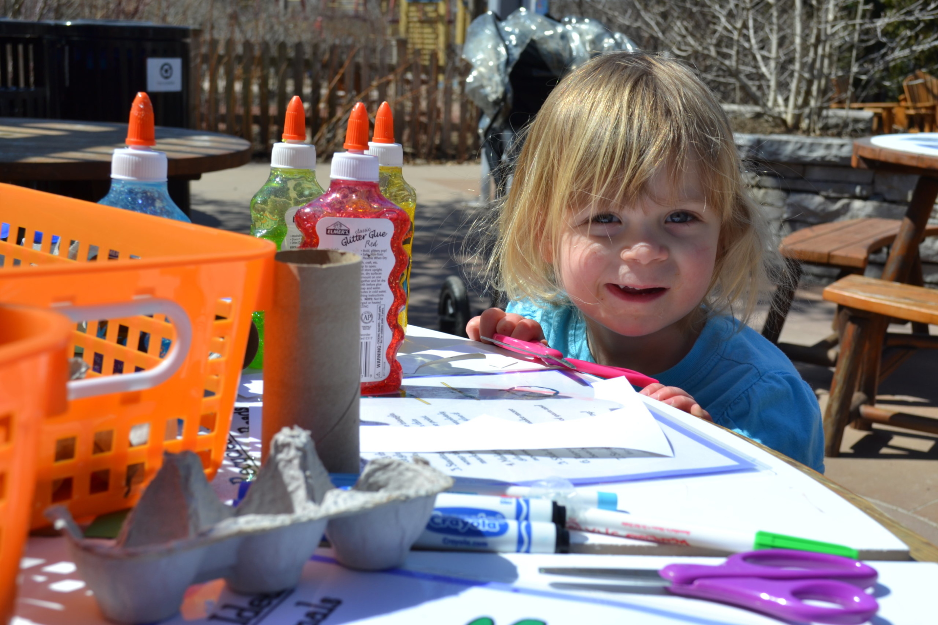 A little girl sitting at a table full of art supplies in the children's garden.