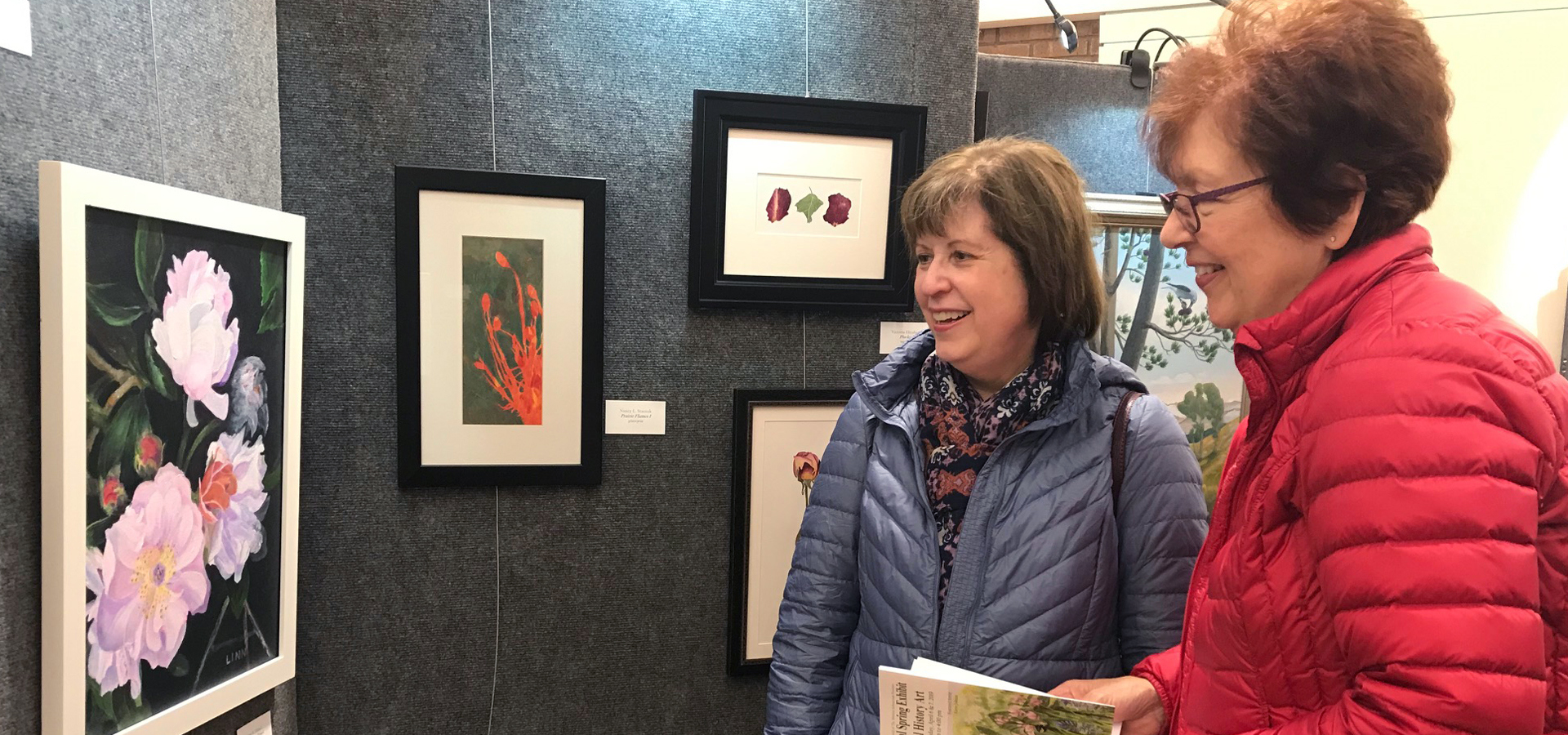 Two women admire paintings at the Nature Artists Guild exhibit