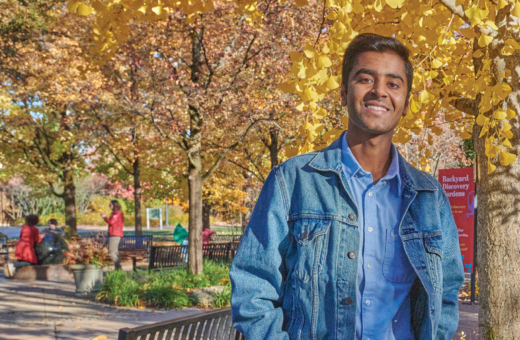 A young man poses in front of a yellow ginkgo tree in the Children's Garden in the fall.