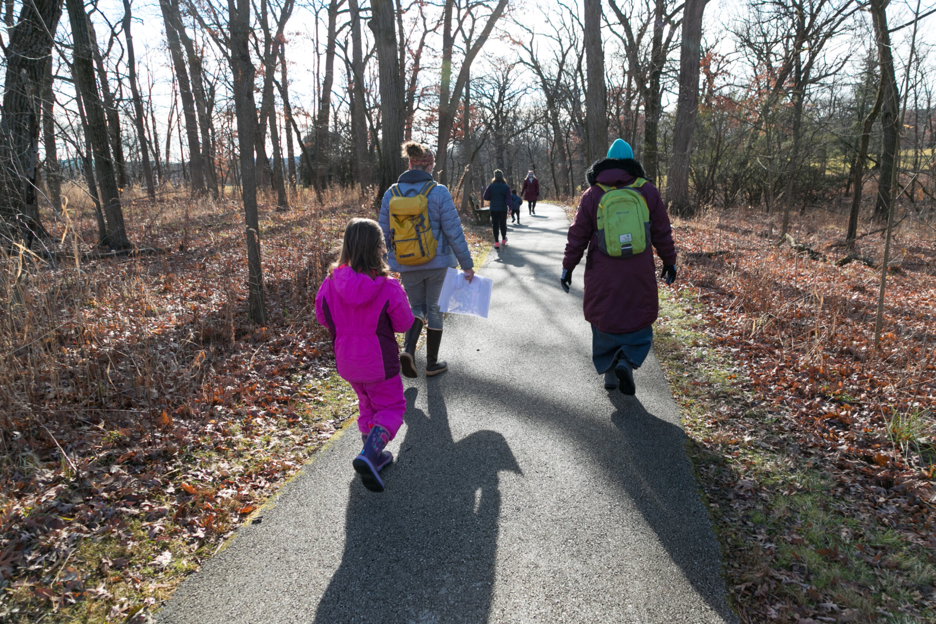 Kids going on a winter hike with instructors on a paved path through the woods.