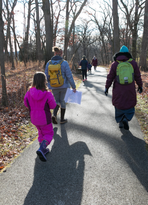 Kids going on a winter hike with instructors on a paved path through the woods.