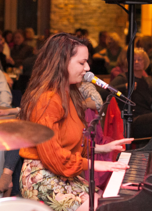 Woman plays piano and sings in front of guests at a dueling piano event
