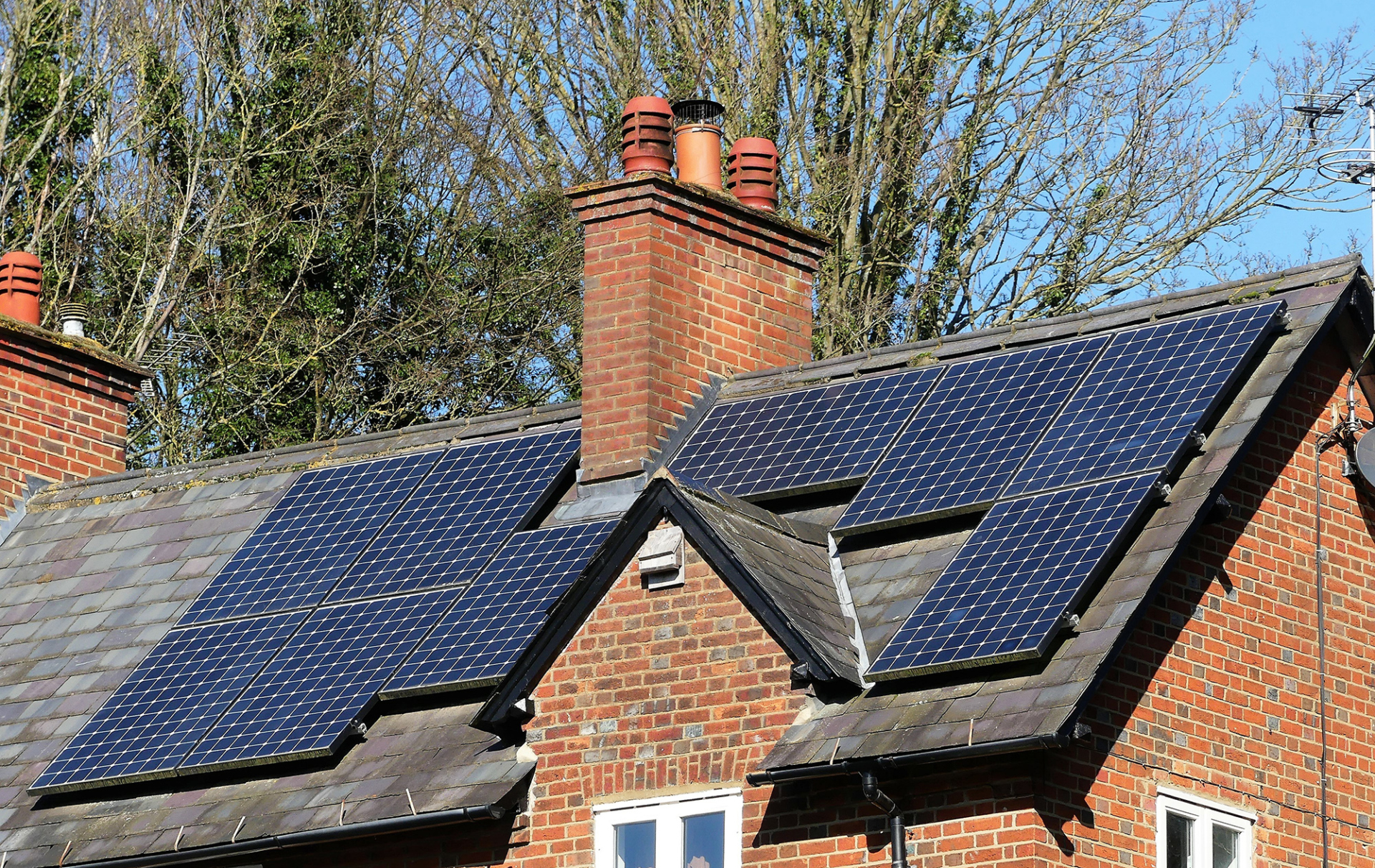Solar panels installed on the roof of a home with large trees in the background.
