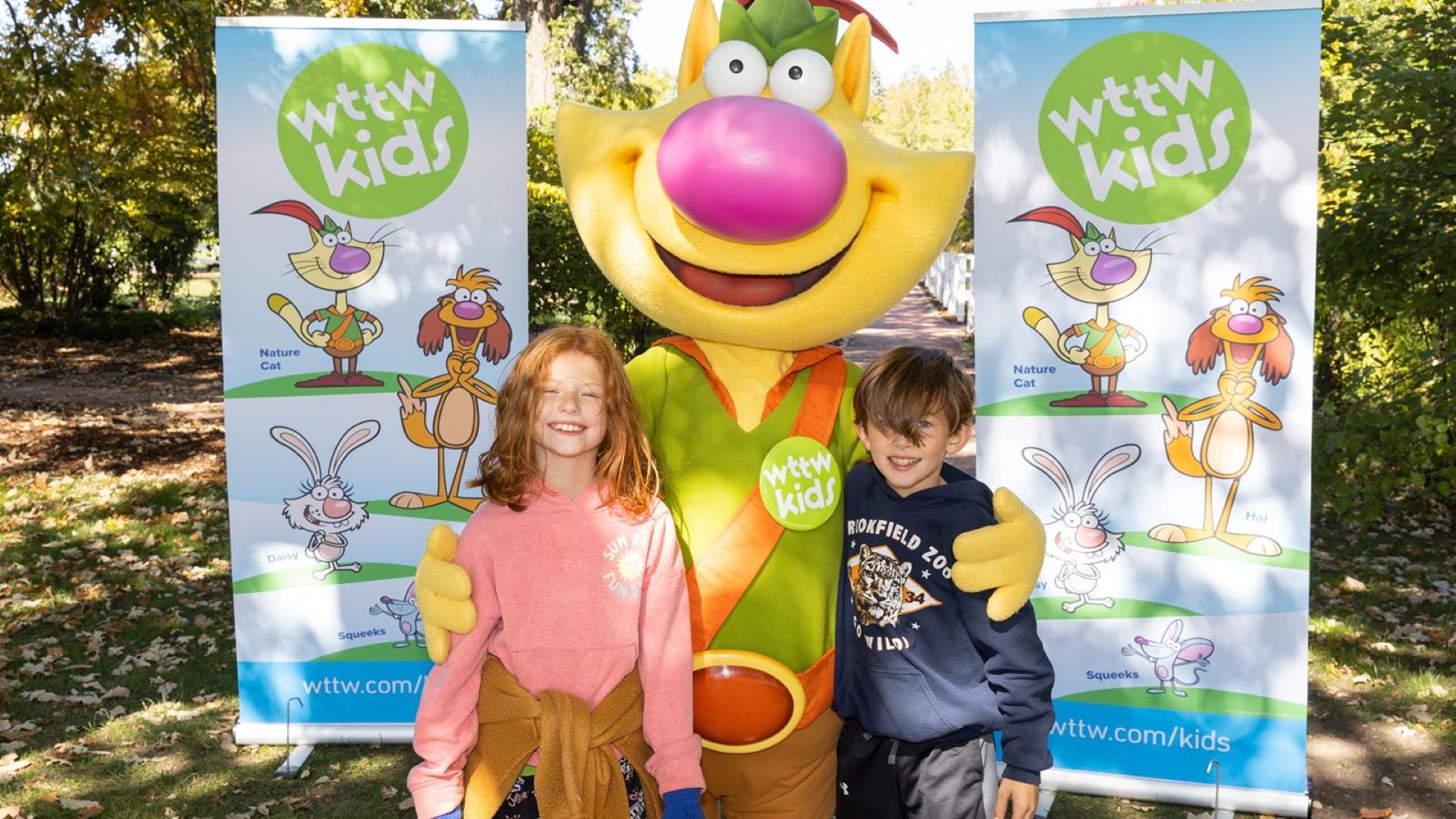 Two young children get a hug from Nature Cat