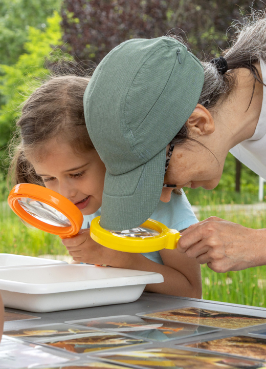 A mother and daughter inspect pond specimens through microscopes together in the Children's Garden