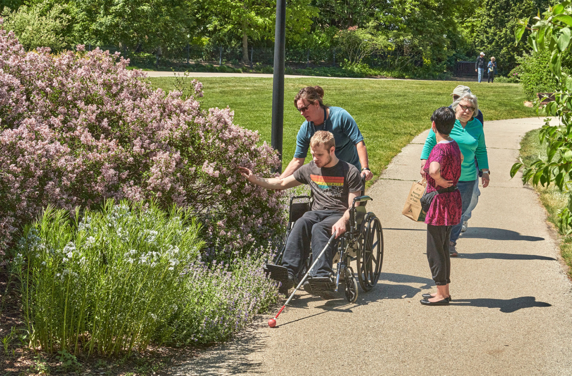 A guest in a wheelchair that is vision impaired touches the flowering bushes around Meadow Lake