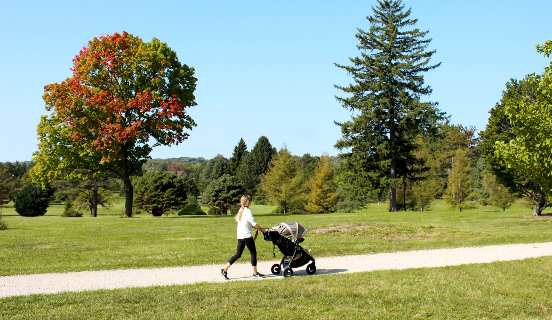 A woman walking on a paved path with a stroller in early fall.