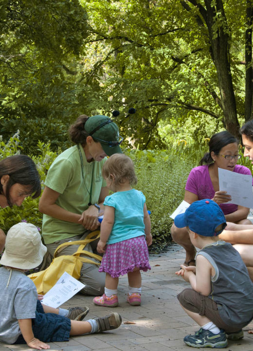 A group of moms and toddlers taking a class outdoors in the Children's Garden