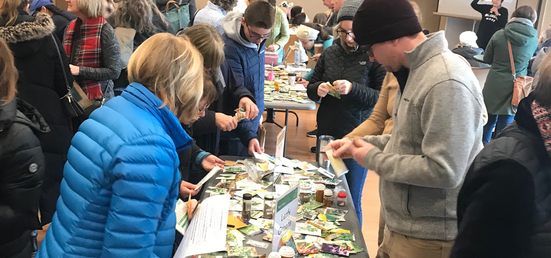 People crowded around a table containing seeds for leafy greens at a seed swap event.