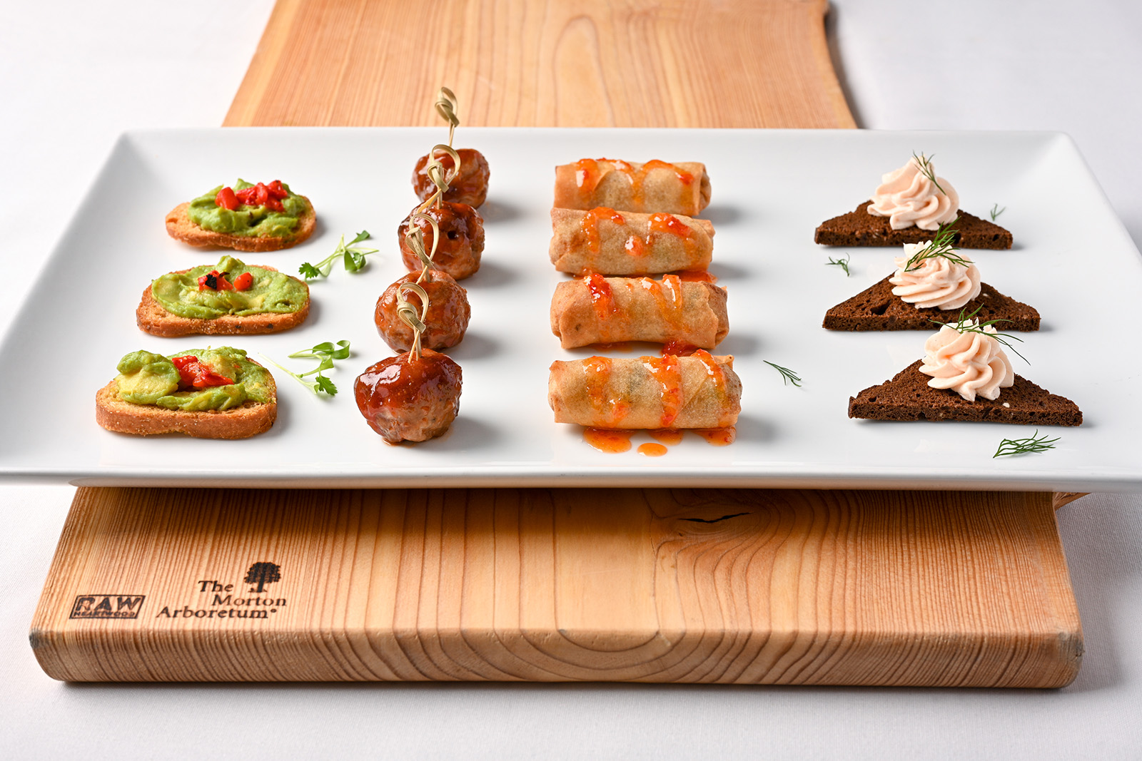 Four appetizer options on a white plate sitting on top of a wood cutting board