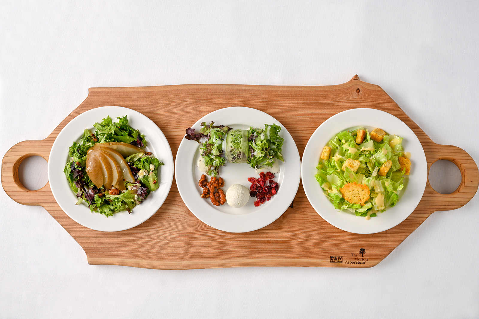 Three plated salads sitting on a wooden cutting board on a white background