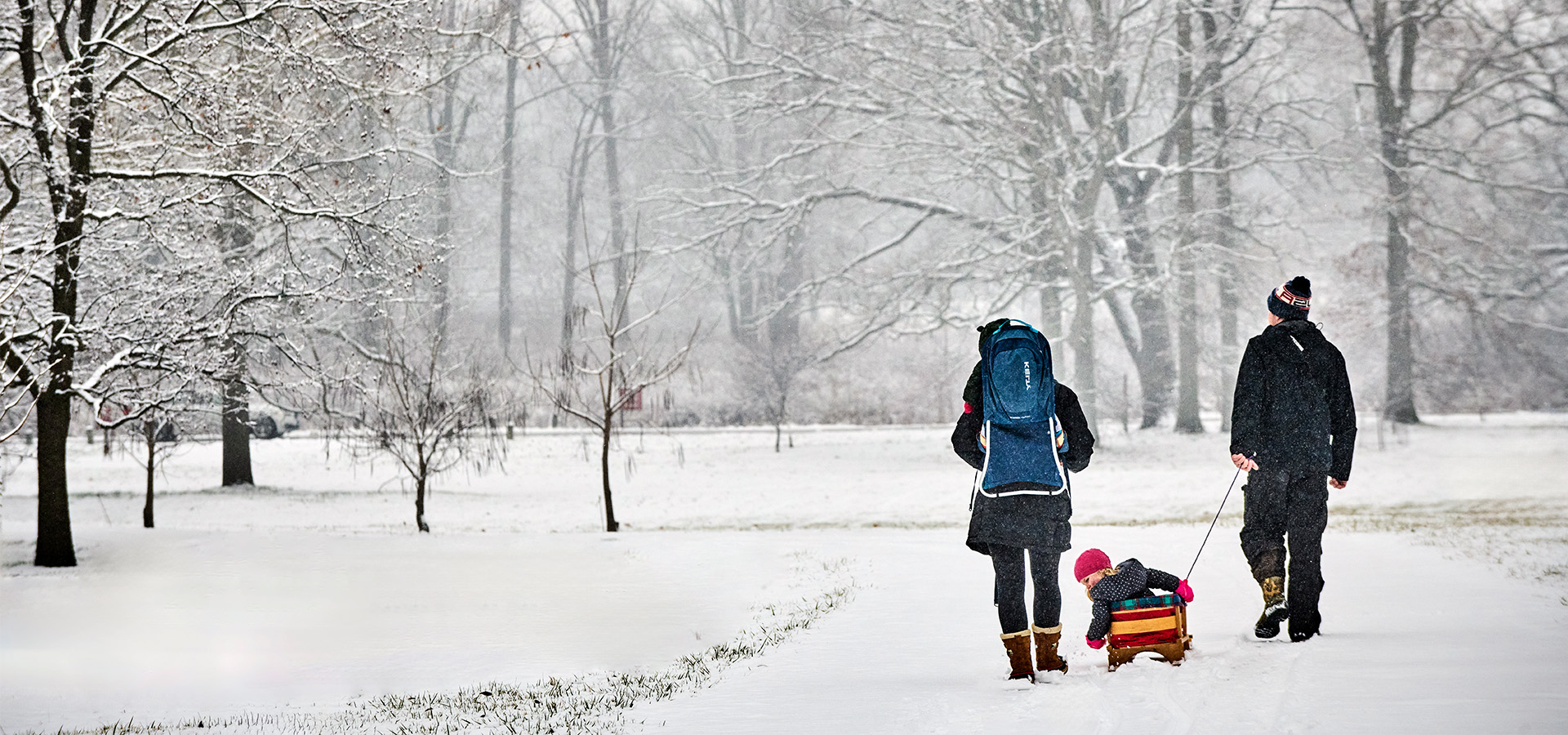 A young family walking on a snowy path, pulling a young child in a sled.