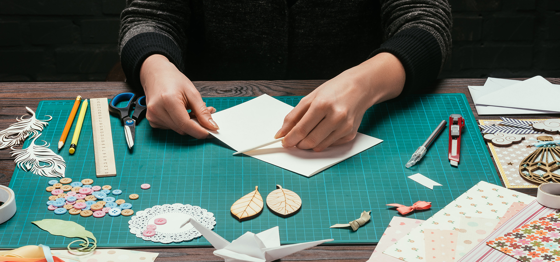 A photographs of a craft maker using a gridded table and tools to craft handmade cards