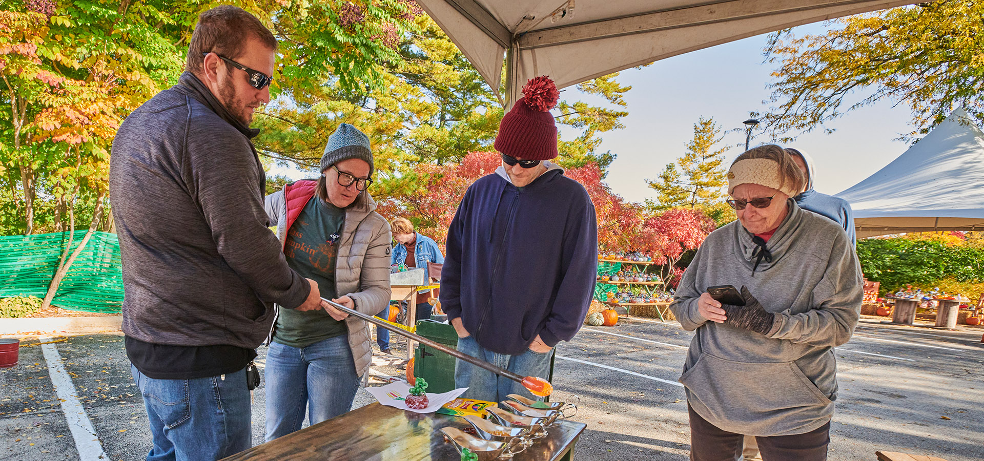 A group of visitors watches a glass blowing demonstration from artists at The Morton Arboretum's Glass Pumpkin Patch