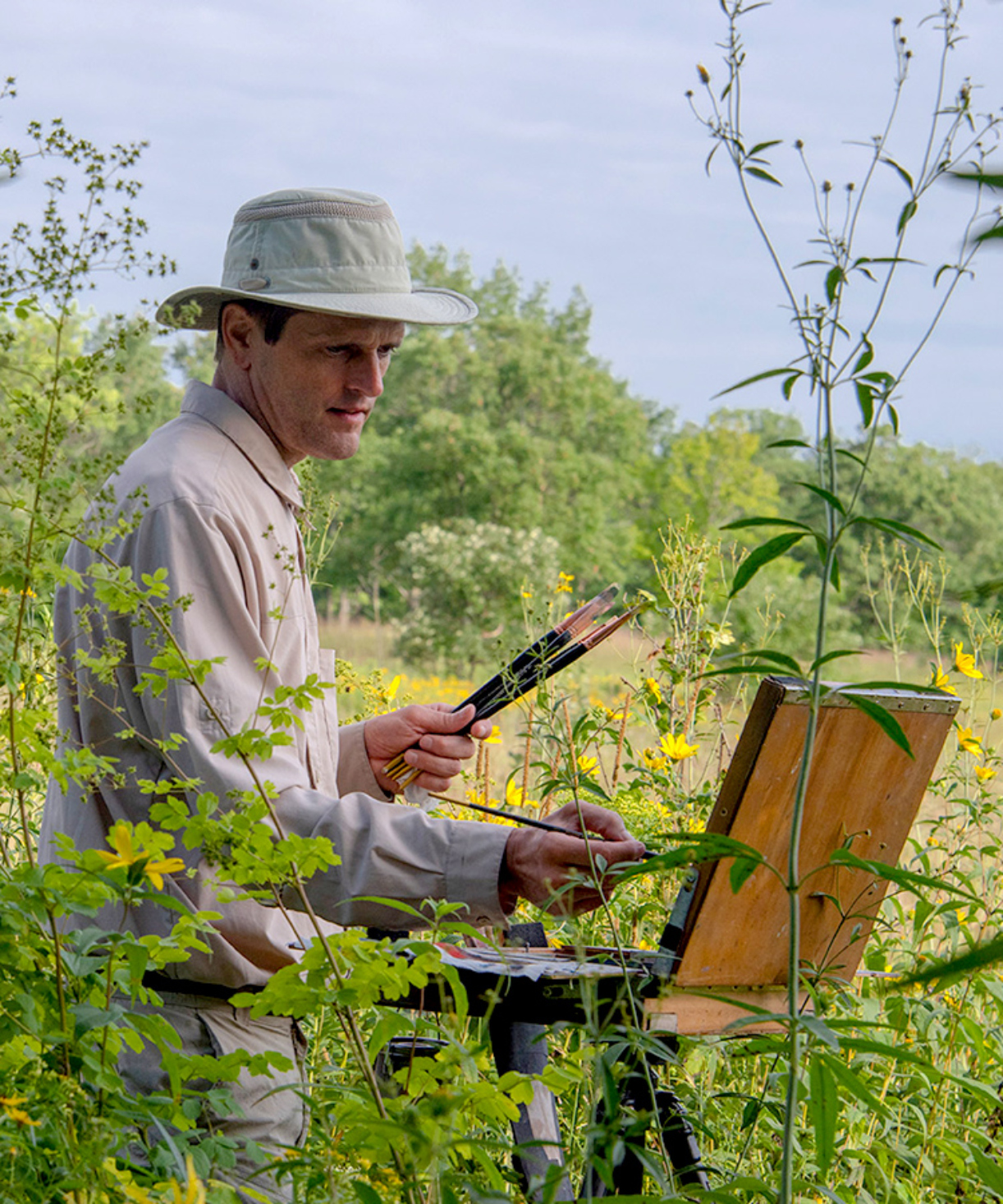 Photograph of artist Philip Juras during a plein air painting within a tallgrass prairie