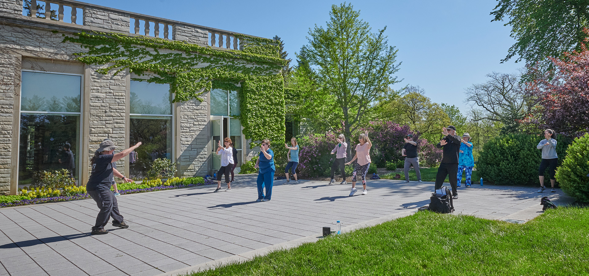 A group doing Tai Chi exercise on the patio of the Thornhill Education Center at The Morton Arboretum