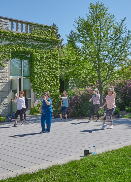 A group doing Tai Chi exercise on the patio of the Thornhill Education Center at The Morton Arboretum