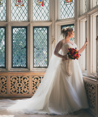 Bride holding a bouquet stands at the window in the Founder's Room
