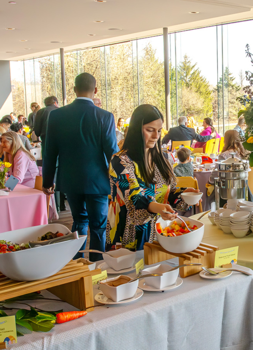 Visitors in a buffet line and sitting at tables in the Ginkgo restaurant. The restaurant is decorated with flowers and pastel colors for Easter.