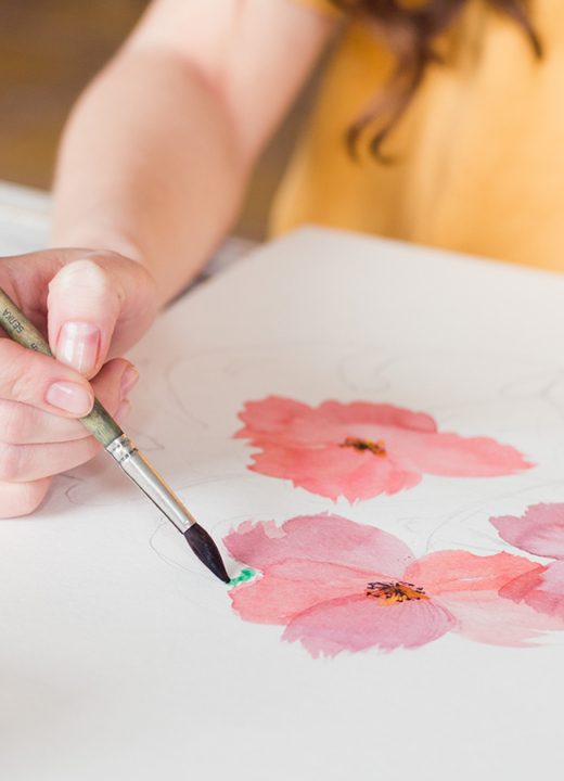 Overhead photo of a woman painting pink flowers with watercolors.