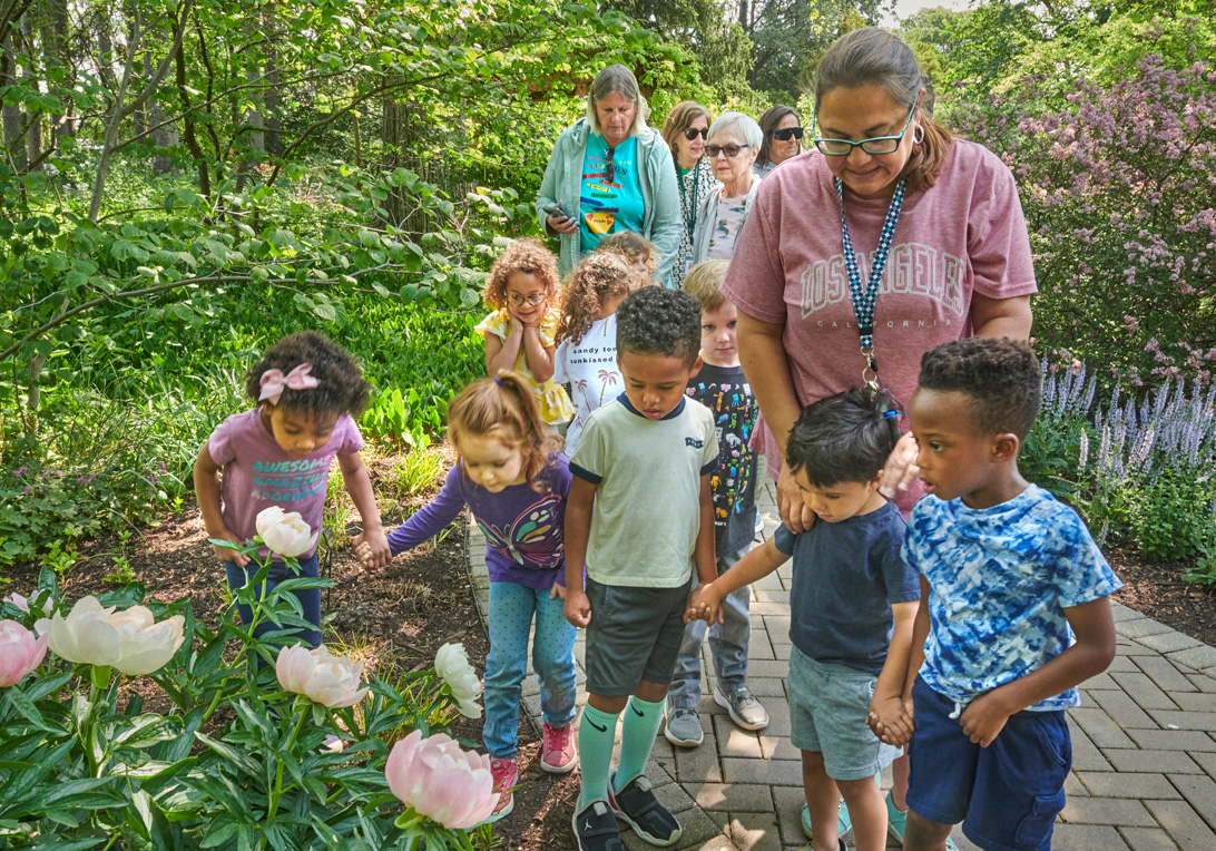 A group of adults and young children smell peonies that are blooming in the Fragrance Garden in spring.