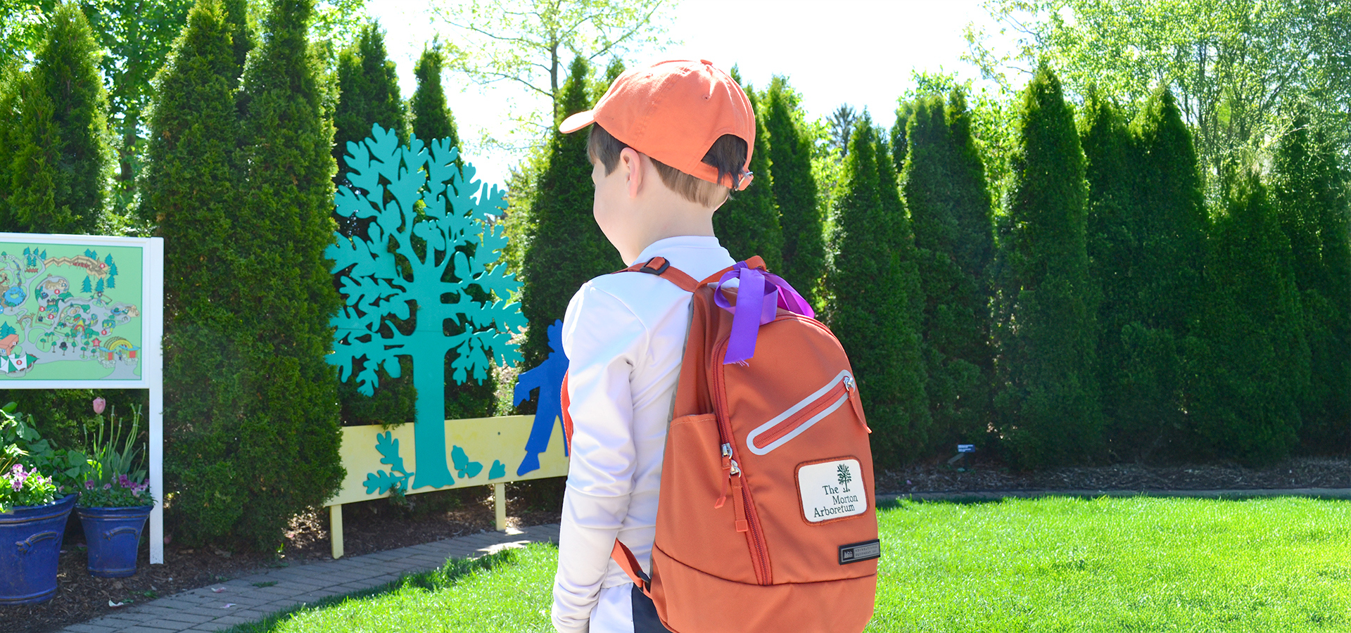 A child wearing an orange ball cap and orange backpack walks into the Children's Garden.