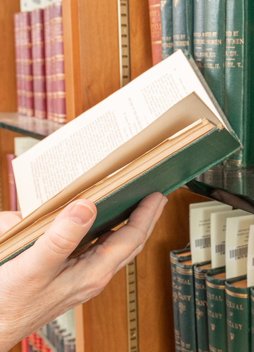Close of of hands holding an old book open in front of a bookshelf.