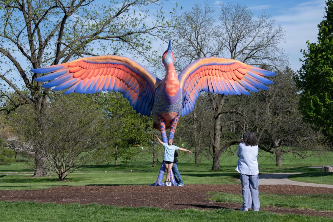 A person photographs a child standing with arms outstretched in front of Cadence the sandhill crane