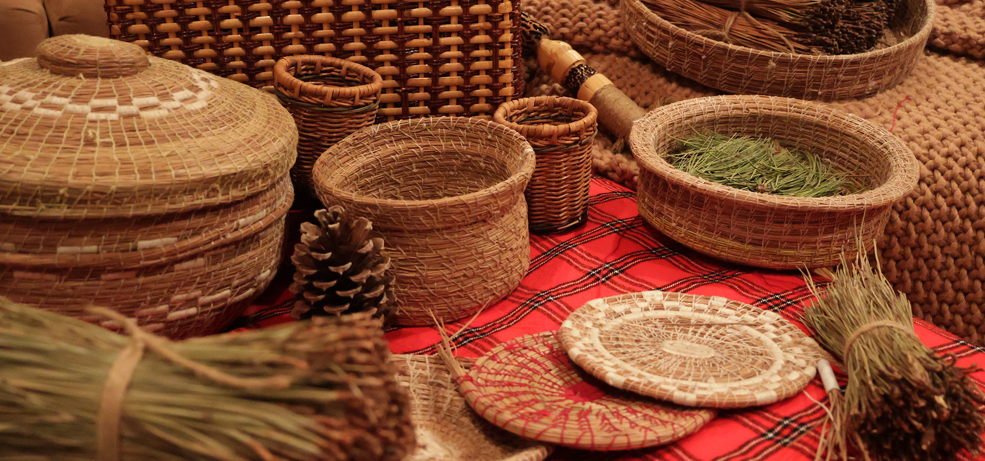 Woven pine needle baskets of varying size and shape displayed on a red tartan cloth.