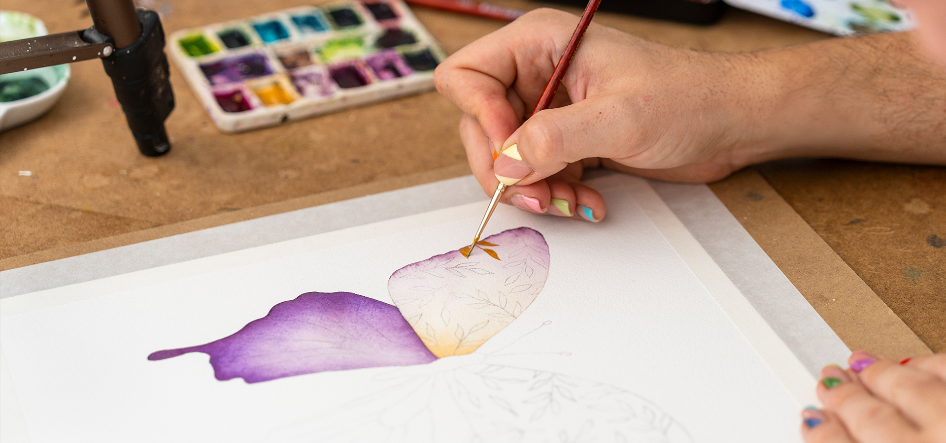 Artist uses a fine brush to add decorative detail to a painting of a butterfly using watercolors.