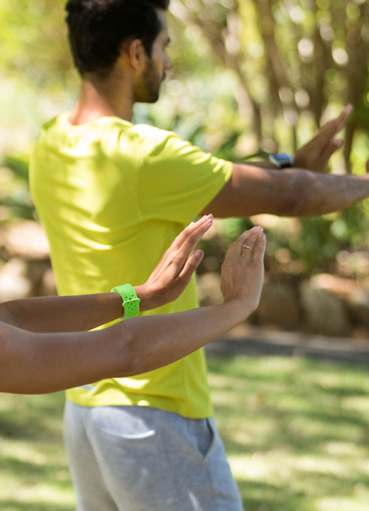 People participate in an exercise class in a grassy area with trees in the background
