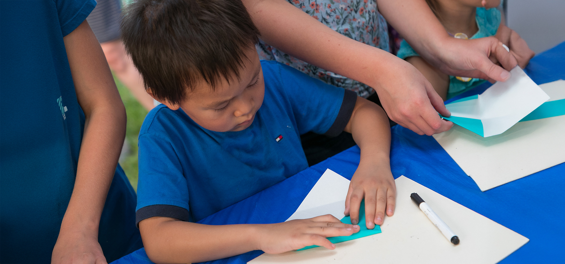 A young boy folding a piece of blue origami paper.