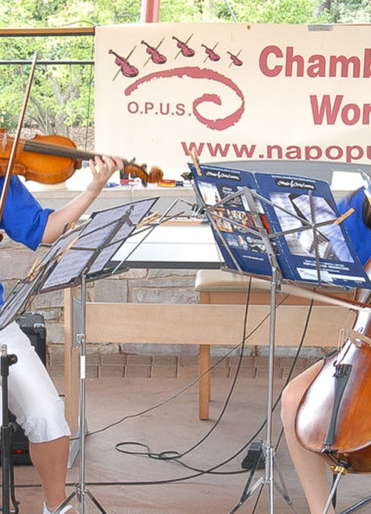 Four young musicians from OPUS Chamber Music Camp seated in front of music stands, performing outdoors as a string quartet.