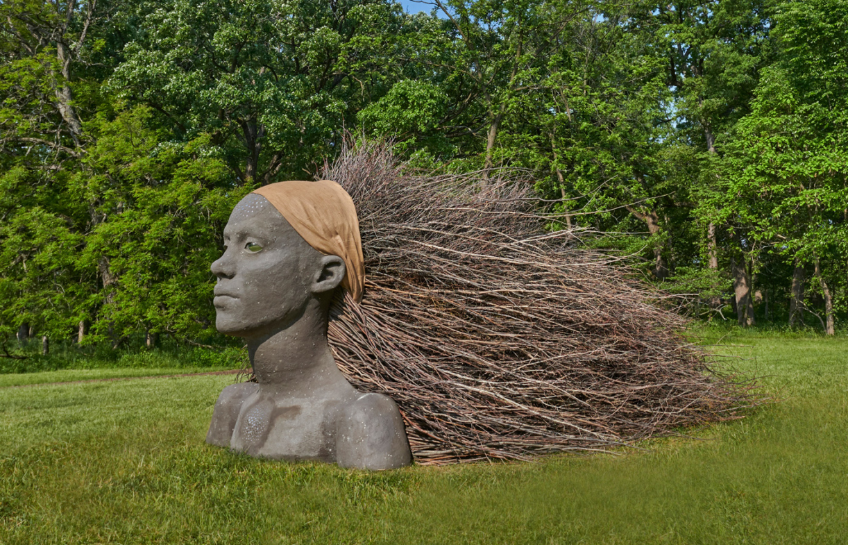 Sculpture of a woman's head and shoulders, with hair made of sticks blowing behind her