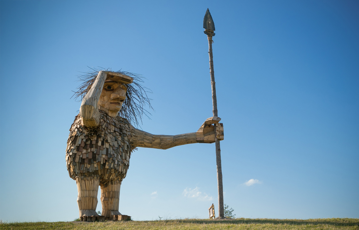 Troll sculpture holding a spear, shading his eyes as he surveys the landscape from the top of a hill
