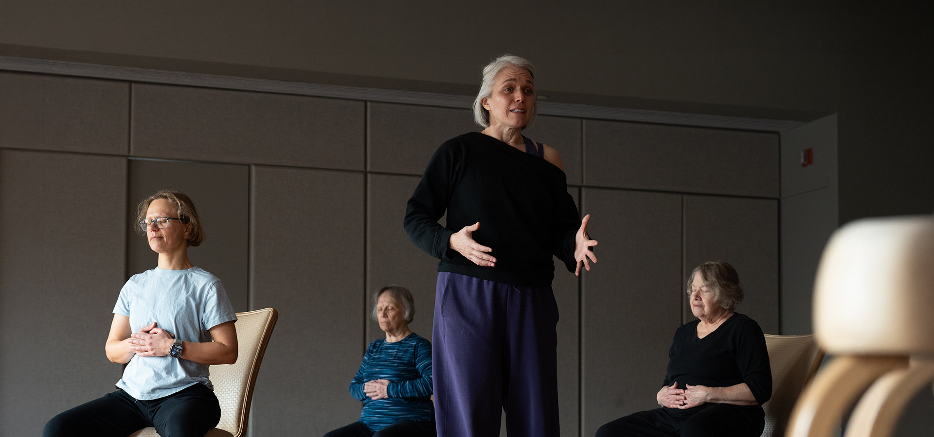 Photograph of a mobility instructor leading seated practitioners in a mindful mobility stretch