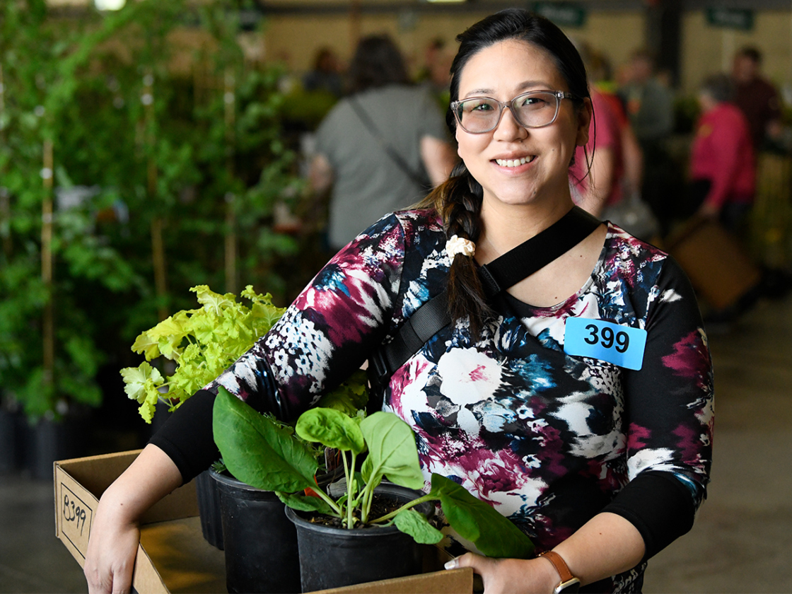 Photograph of a woman customer wearing a floral shirt holding a box of plants purchased at The Morton Arboretum's Arbor Day Plant Sale