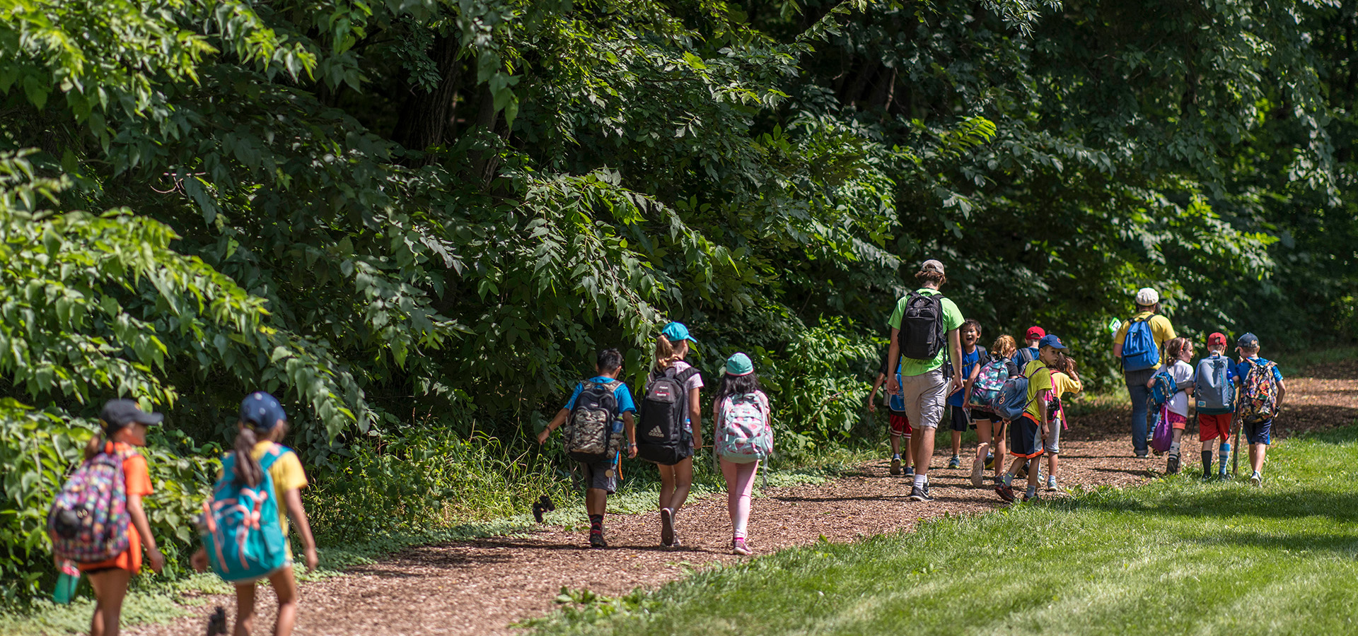 A photograph of schoolchildren walking along with camp instructors on a chipped hiking trail at The Morton Arboretum