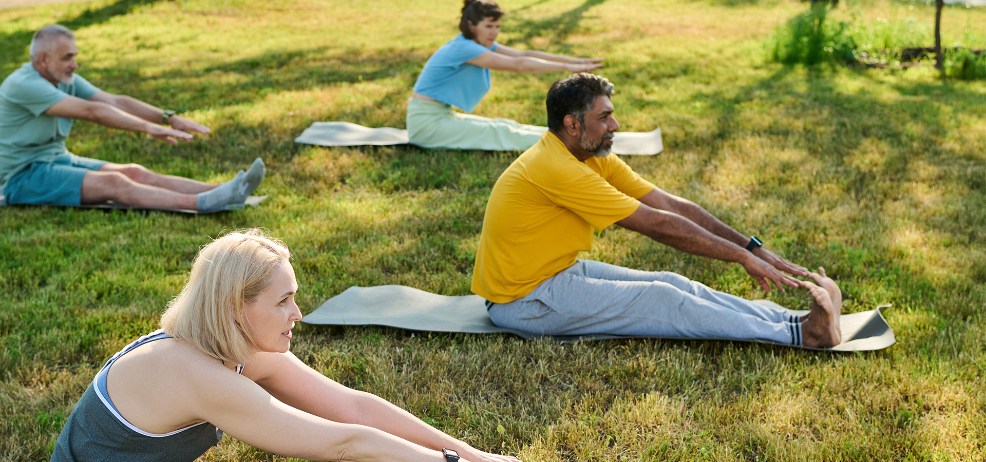Photograph of adults stretching on yoga mats outdoors on a green lawn