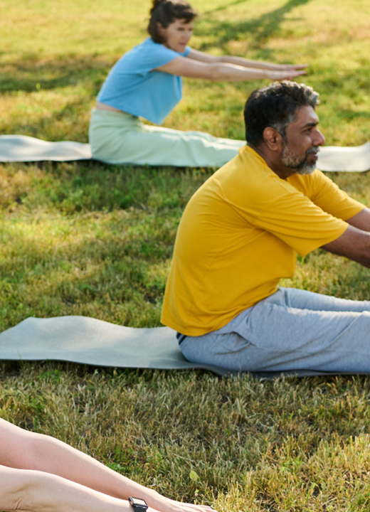 Photograph of adults stretching on yoga mats outdoors on a green lawn