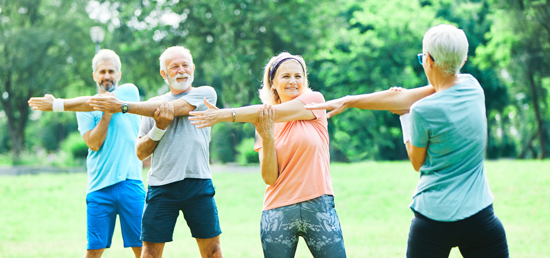 Photograph of three adults stretching their arms alongside an instructor