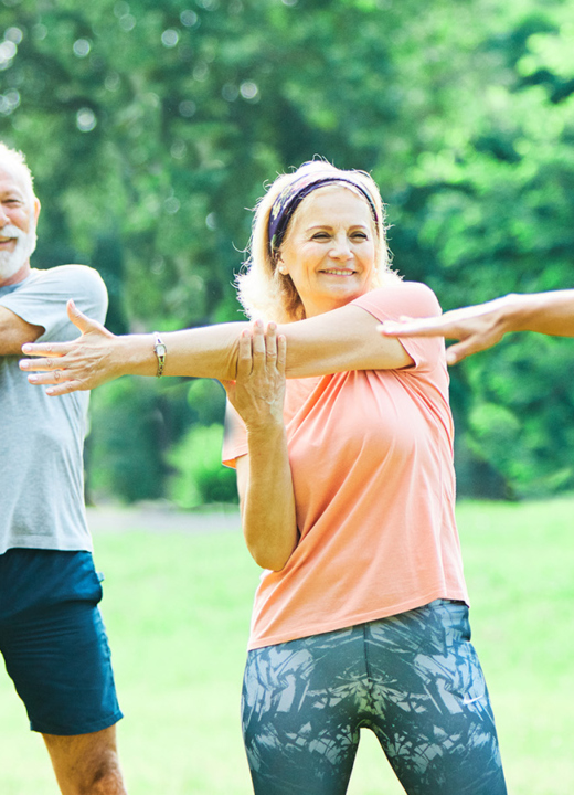 Photograph of three adults stretching their arms alongside an instructor