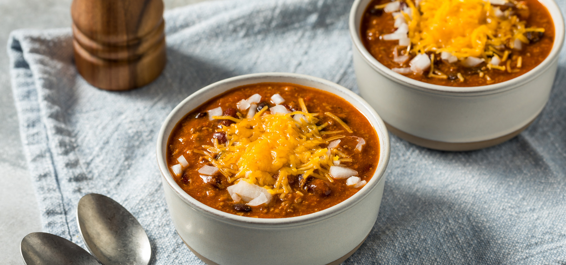 An image of bowls of chili with toppings on a napkin with spoons.