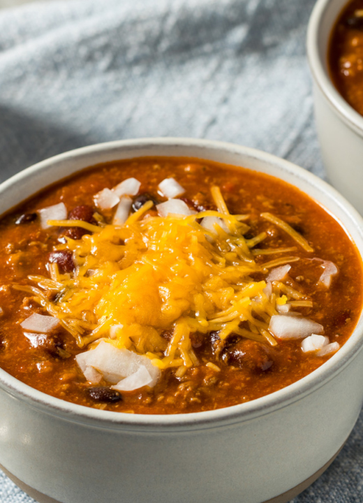 An image of bowls of chili with toppings on a napkin with spoons.