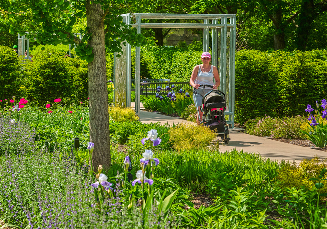 A woman walks with a stroller in The Grand Garden with stunning flowers all around