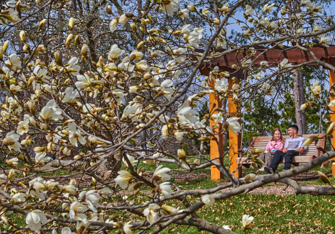 A couple relaxes on a swing in the Magnolia collection with white blooms all around them