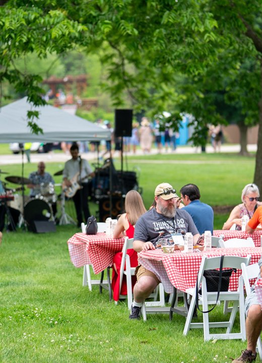 Photograph of visitors at the Blues, Brews, and BBQ event sitting at tables eating BBQ