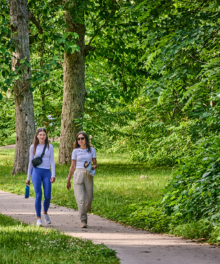 Image of two young women walking on a paved trail at the Morton Arboretum during summer with green foliage surrounding them
